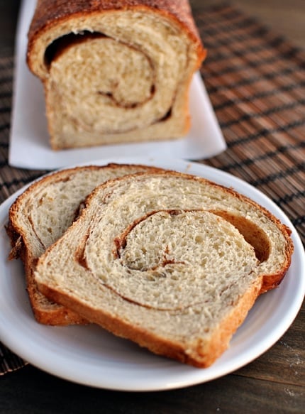 Two pieces of cinnamon swirl bread on a white plate with the rest of the loaf behind it.