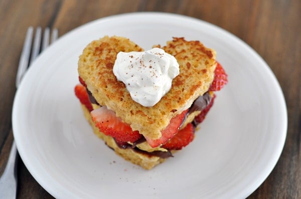 Top view of a heart shaped chocolate and strawberry stuffed french toast on a white plate.