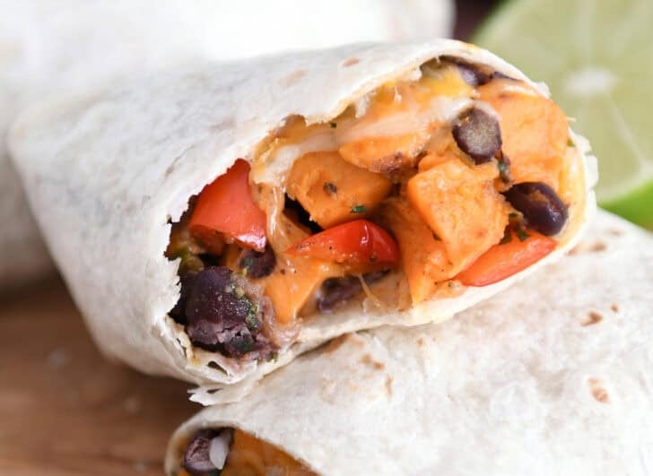 Two halves of sweet potato burritos with one bite removed.