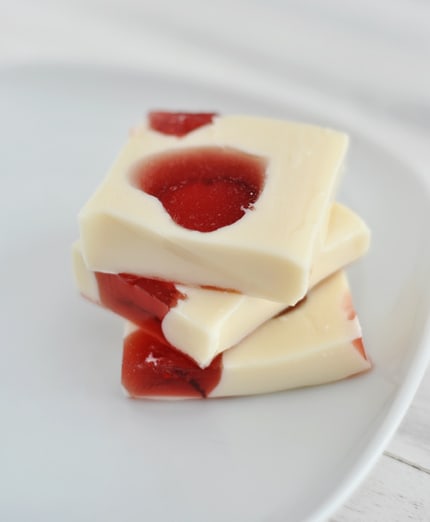 Three squares of white Jello with red Jello hearts inside on a white plate stacked on top of each other.