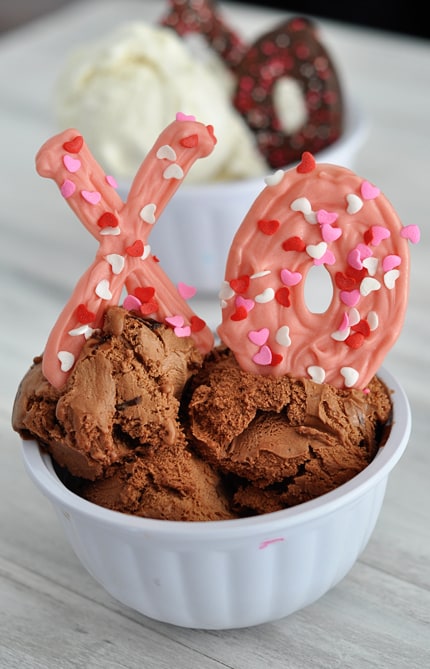 White bowl with chocolate ice cream and a pink chocolate sprinkled X and O nestled in the ice cream.