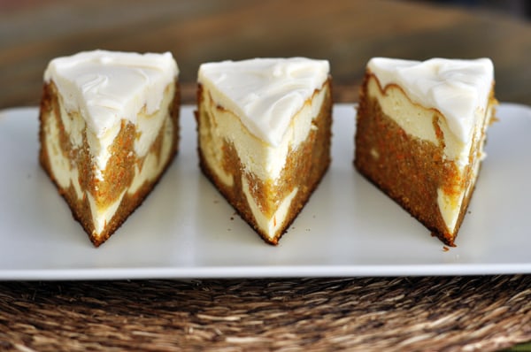 Three pieces of carrot cake cheesecake, topped with white frosting, on a white plate.