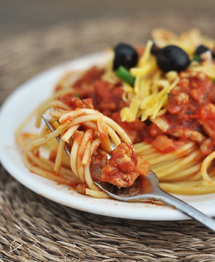 Plate full of spaghetti topped with sauce, cheese, and black olives.