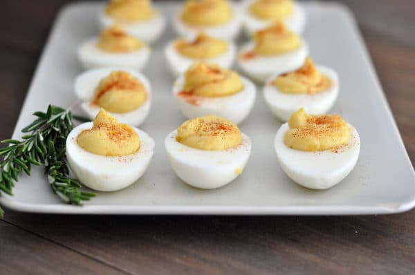 Top view of a white tray of deviled eggs with a sprig of rosemary on the side.