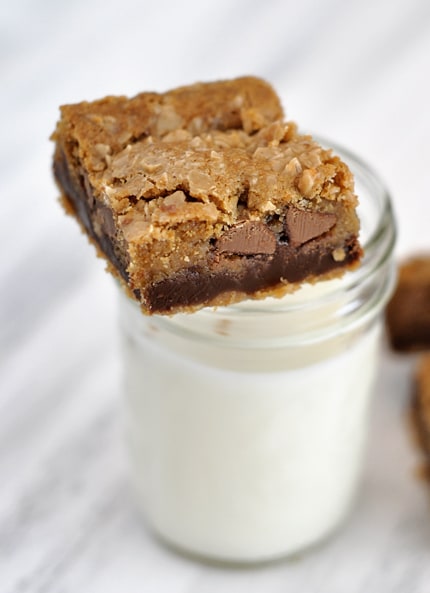 A fudge filled chocolate chip cookie bar laying on top of a mason jar of milk.
