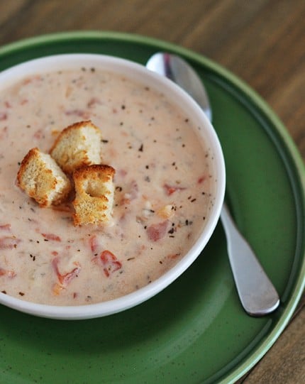 Top view of a white bowl full of tomato basil soup with three croutons in the middle.