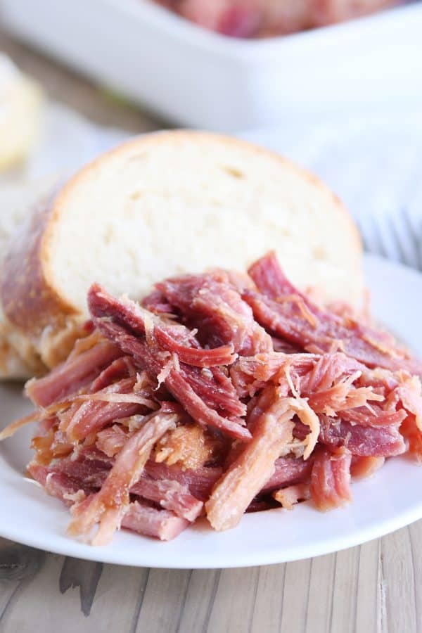 Pile of sweet baked ham on white plate with bread.