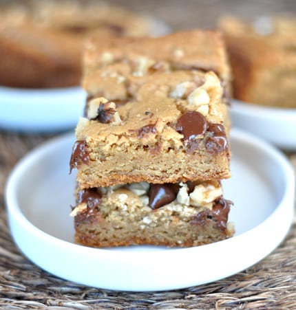 Two walnut and chocolate chip blondies stacked on a white plate.