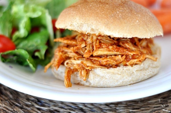 A white plate with a bbq pulled chicken sandwich next to a green salad.