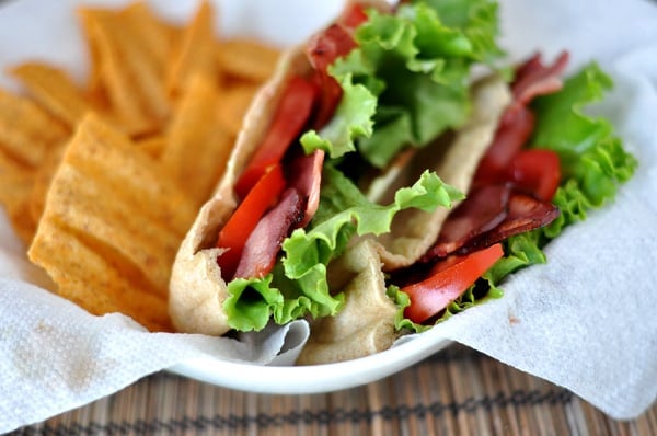 A cut open BLT pita pocket next to some chips in a white paper-lined basket.