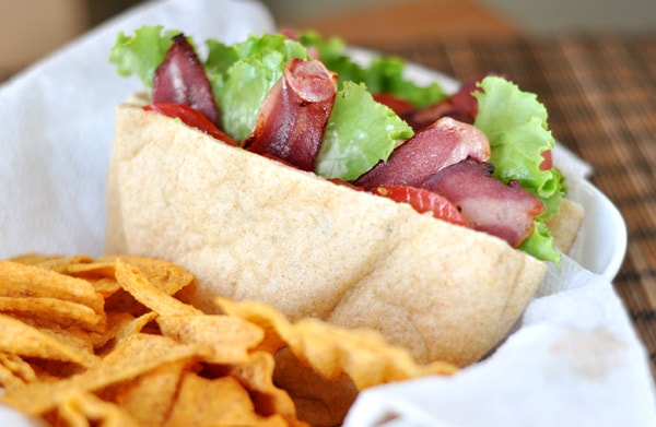 A cut open BLT pita pocket and chips in a paper lined basket.
