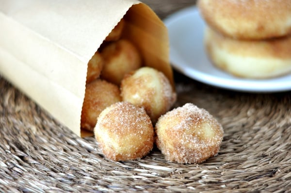 A paper bag tipped on it's side with doughnut holes coming out of the bag.