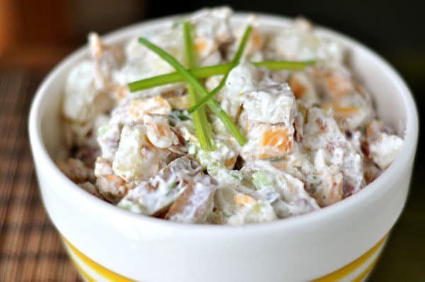 white bowl full of baked potato salad with sprigs of chives on top