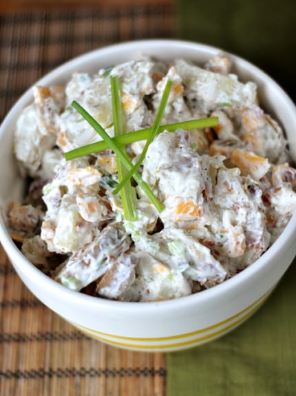 Top view of a white bowl full of baked potato salad with stalks of chives on top.