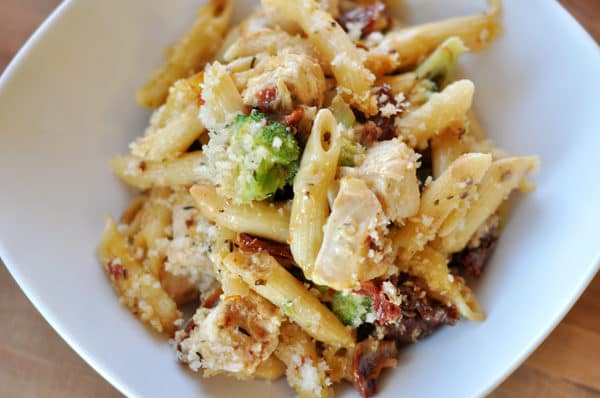 top view of a white dish full of baked penne, chicken, broccoli, cheese, and tomatoes