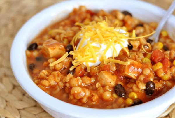 A bowl of red southwest chicken and barley chili topped with sour cream and cheese.