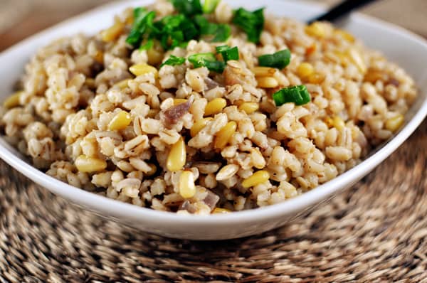 A white bowl with cooked barley and pine nuts.