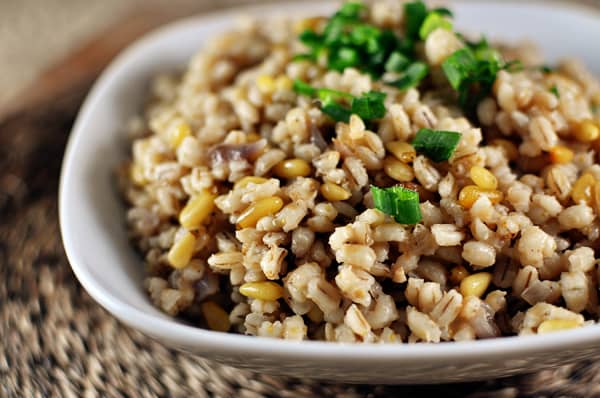 White bowl with cooked barley and pine nuts, and topped with green onions.