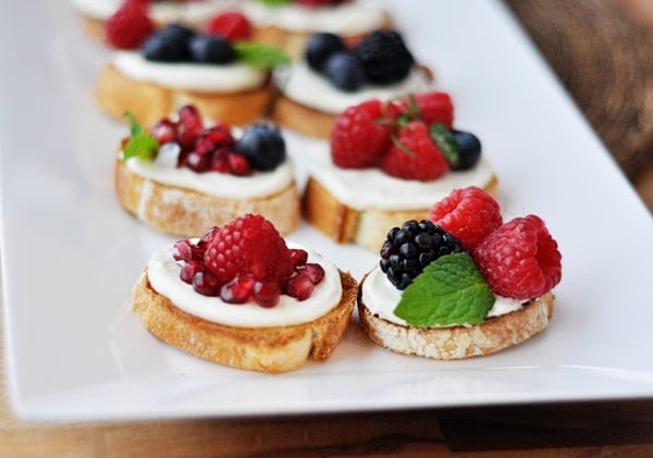 White tray of pomegranate, raspberry, blackberry, and blueberry bruschetta appetizers.