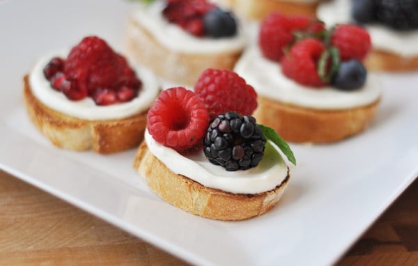 White tray of pomegranate, raspberry, blackberry, and blueberry bruschetta appetizers.