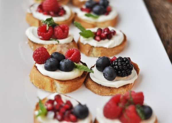 Top view of a white tray of pomegranate, raspberry, blackberry, and blueberry bruschetta appetizers.