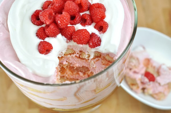 Top view of a berry trifle topped with whipped cream and fresh raspberries with a big scoop taken out of the dish.