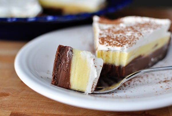 A slice of black bottom pudding pie with whipped topping and a bite taken out on a white plate.