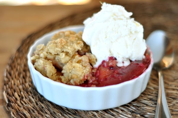 White ramekin with baked nectarine crumble and a scoop of vanilla ice cream.