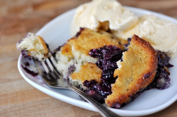 Square white plate with fresh blueberry cobbler and vanilla ice cream on the side.