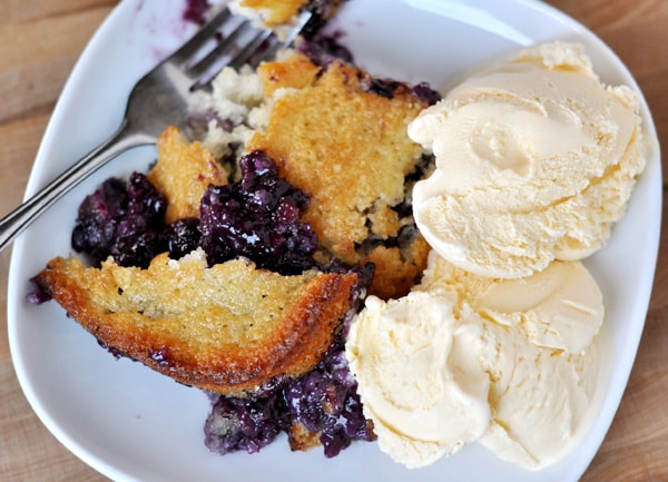 Top view of a white plate with baked blueberry cobbler and vanilla ice cream on the side.