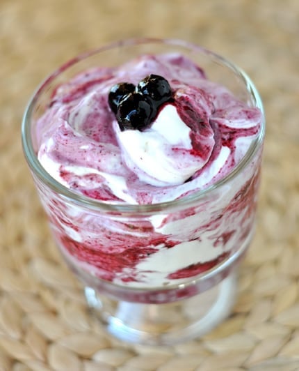 A glass goblet with a blueberry and yogurt mixture topped with a few blueberries.