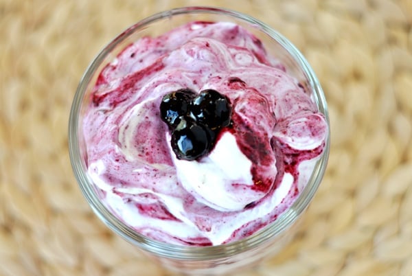 Top view of a swirled blueberry and yogurt dessert in a glass goblet.