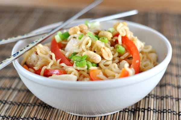 White bowl with noodles, peppers, chicken, and edamame.