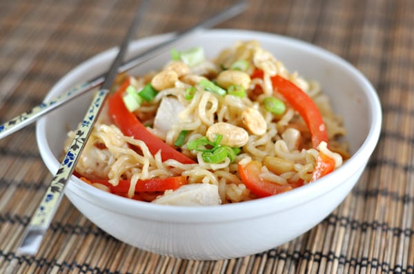 White bowl with noodles, sliced red peppers, chicken, and edamame.