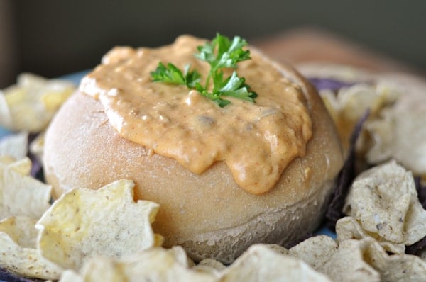 Bread bowl full of chorizo dip with tortilla chips around the bowl.