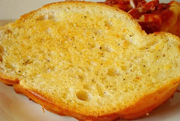 Slice of buttered garlic bread on a white plate.