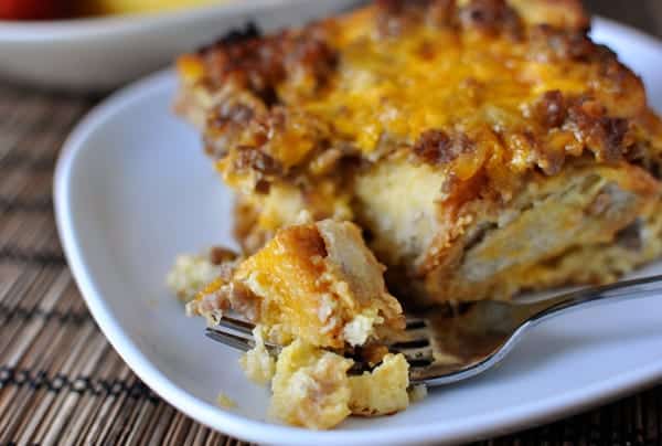 A square piece of sausage and egg breakfast casserole on a white plate with a fork taking one bite out.