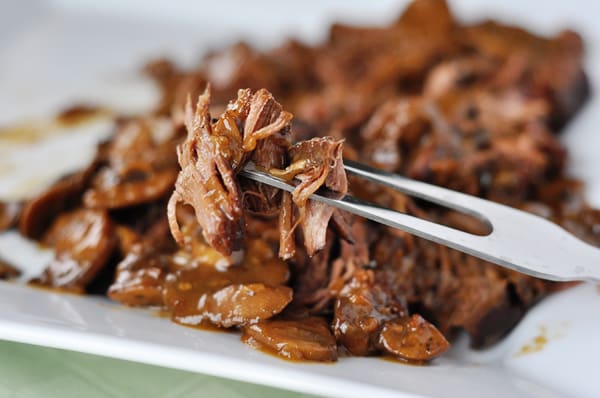 Shredded braised brisket on a white platter with a fork lifting a bite out.