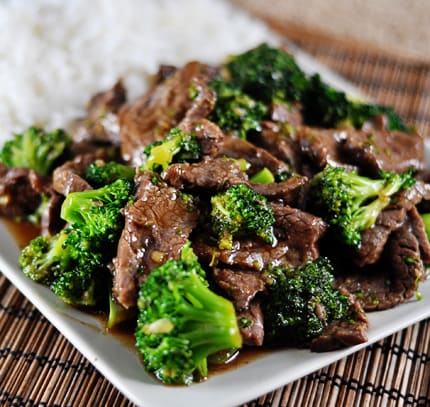 A white platter with cooked broccoli and beef next to cooked white rice.