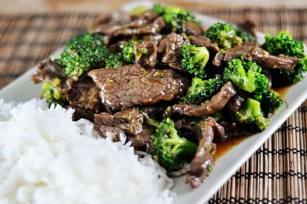White platter with cooked white rice next to cooked broccoli and beef.