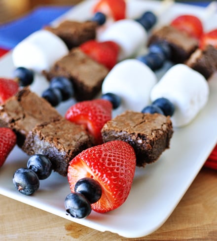 White platter with brownie, blueberry, strawberry, and marshmallow kebabs.
