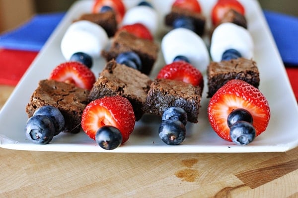 White platter with four brownie, marshmallow, and fruit kebabs laying side by side.