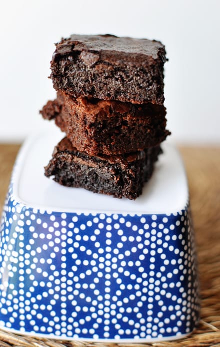 A blue and white designed tupperware turned upside down, with three brownies stacked on top.