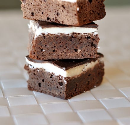 Fudgy brownies with layers of white and chocolate frosting stacked on top of each other.