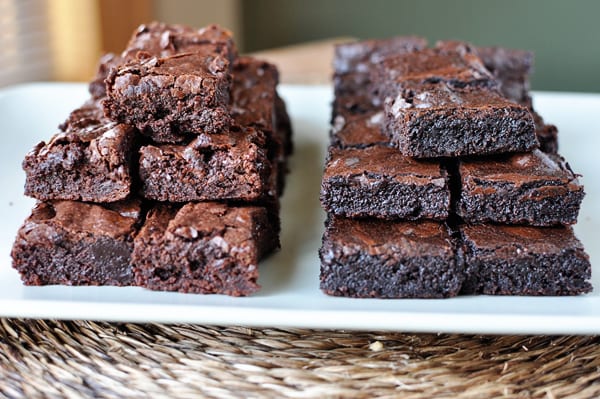 A white plate with two stacks of different kinds of brownies. The stack on the left is lighter brown than the stack on the right.