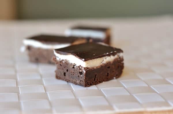 Three fudgy brownies with a middle layer of white frosting and topped with chocolate ganache.