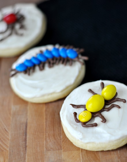 Sugar cookies with white frosting and chocolate bugs on top.