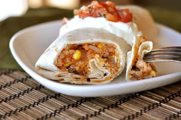 Cut open bean burrito with sour cream and salsa on a white plate.
