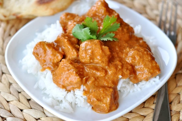White dish with white rice and chicken with Indian butter sauce on top.