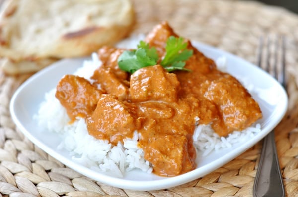 A white dish with rice and Indian chicken and sauce on top.